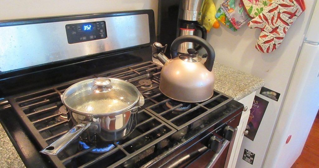 Gas range with a pot and kettle on the burners and the oven clock lit