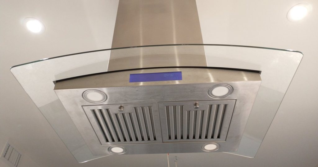 Island range hood with a glass canopy, stainless steel baffle filters and LED lights, seen from below