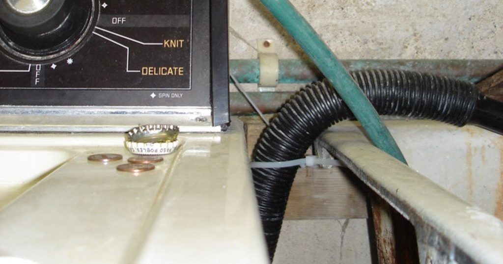 Black ribbed washing machine drain hose looping over a laundry tub behind a top-load washer