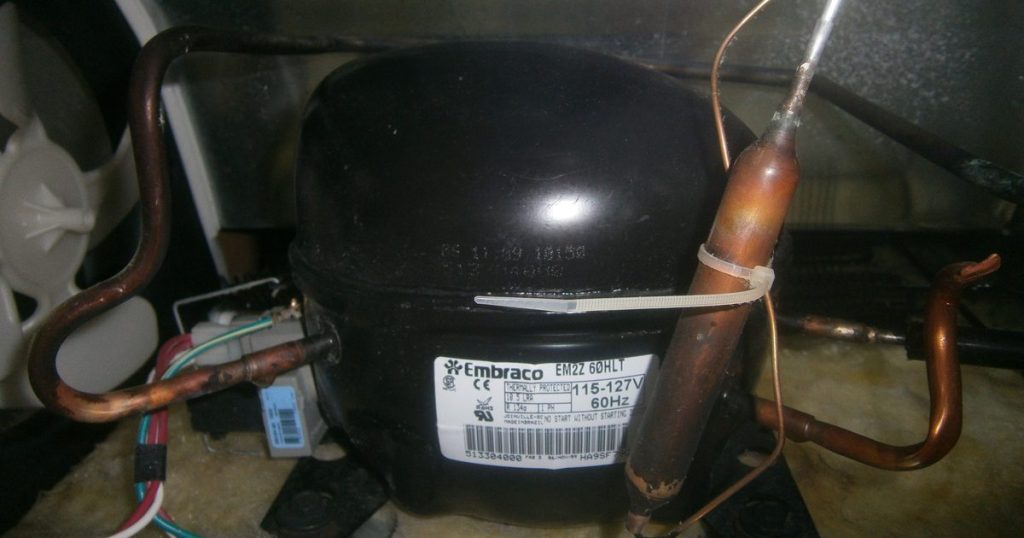 Black Embraco compressor and copper tubing in the rear compartment of a top-freezer refrigerator
