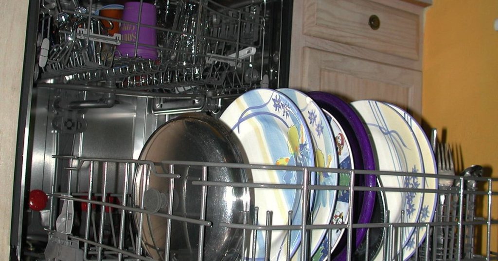 Open dishwasher with plates and a pot lid loaded upright in the bottom rack