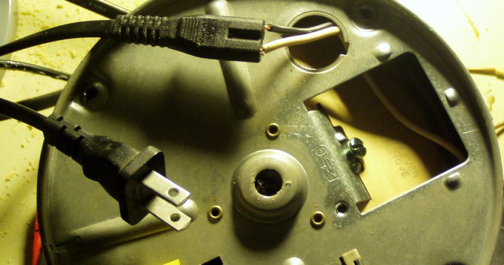 Underside of a garbage disposal with its power cord and wiring cover, partly taken apart