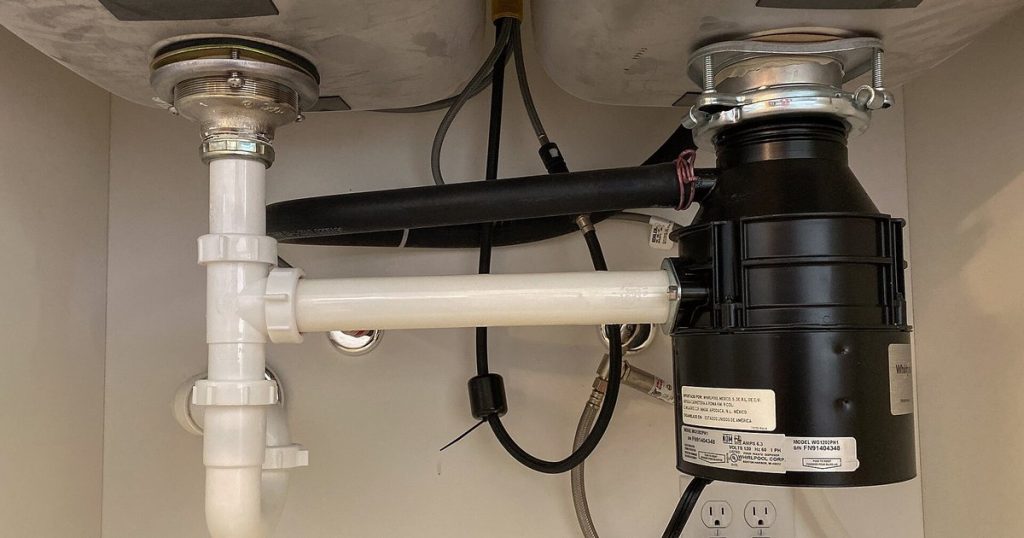 Garbage disposal mounted under a double kitchen sink, with the drain pipe and dishwasher hose connected