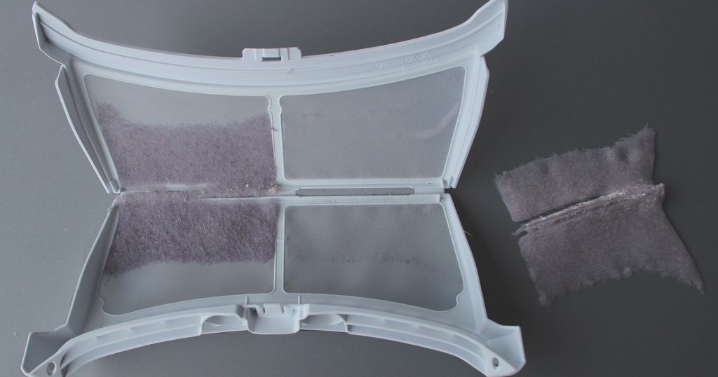 Opened dryer lint screen with a layer of grey lint peeled off and set beside it