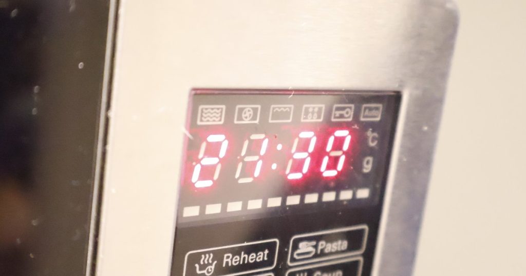 Close-up of a microwave control panel with a red digital clock display and Reheat and Pasta buttons