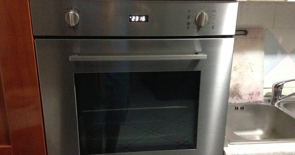 Stainless steel electric convection wall oven with a digital display, set into wood kitchen cabinets