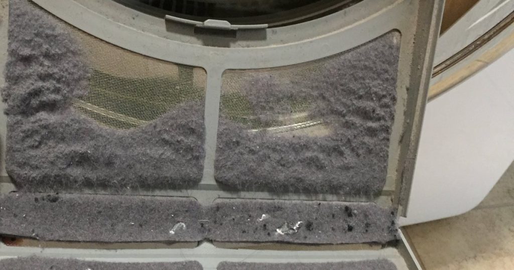 Fold-out dryer lint screen caked with a thick layer of grey lint