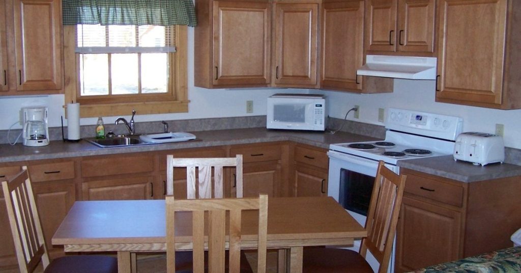 Kitchen with a white countertop microwave on the counter beside an electric range with an under-cabinet range hood