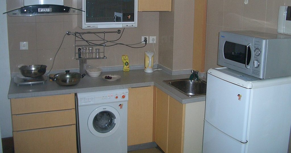 A countertop microwave sitting on top of a small white two-door refrigerator in a compact apartment kitchen