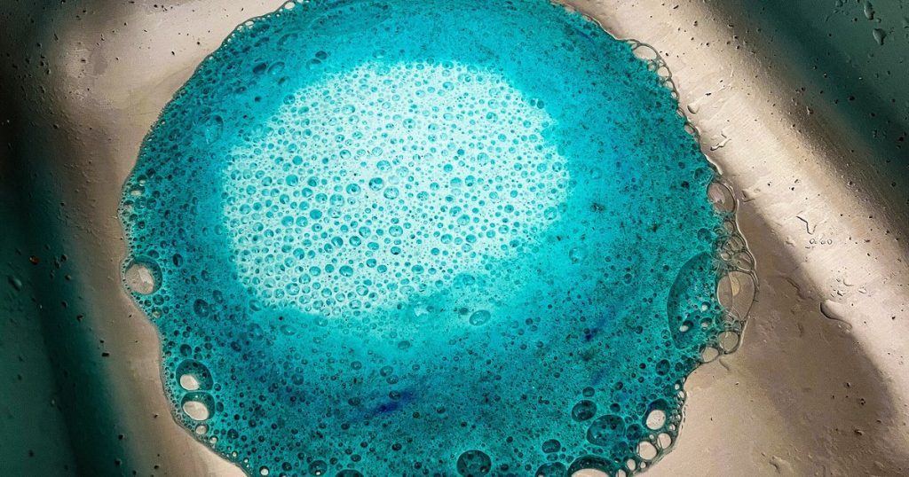 Blue foaming garbage disposal cleaner covering the drain of a stainless steel kitchen sink