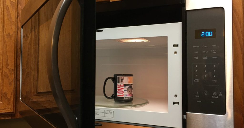 Over-the-range microwave with its door open and a mug on the glass turntable