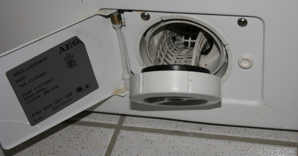 Open access door at the bottom front of a front-load washing machine with the drain pump filter partly unscrewed