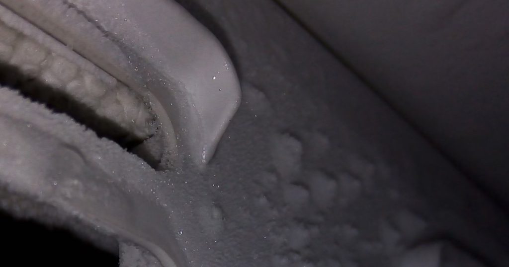 Thick frost covering the air vents and back wall inside a freezer that needs defrosting