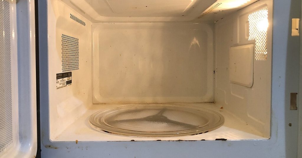 Inside of a dirty microwave with food stains on the walls and glass turntable